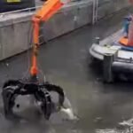 Floating crane (boat w/claw) removes discarded bicycles from water channel.